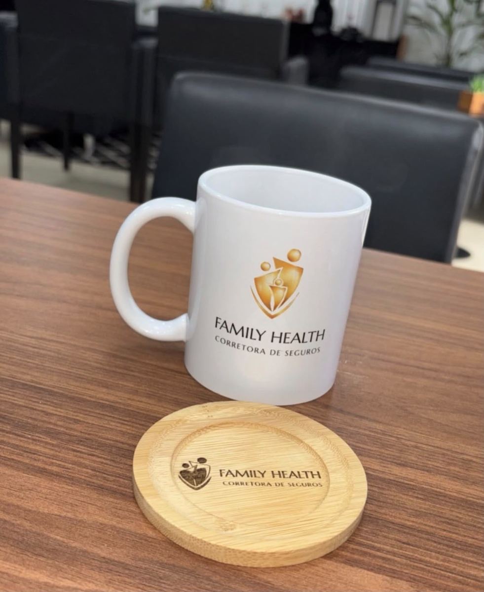 Caneca de cerâmica branca personalizada com a logo de uma corretora de seguros, ao lado de porta-copos de bambu gravado